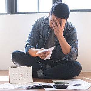 A man, appearing worried, sits on the floor with his head in his hands, reflecting Debt Settlement